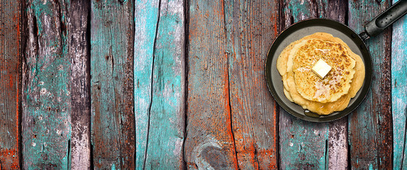 Fototapeta na wymiar Hot delicious pancakes in frying pan on multicolored wooden table. Pancake week. Panoramic banner.