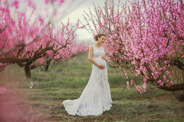Obraz na płótnie Canvas A woman in a long white wedding dress among the peach blossoming trees.