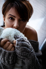 Portrait of good looking 45s years old brunette woman sit on the home floor by the window. Pretty model dressed knitted grey cozy sweater ana look to the window