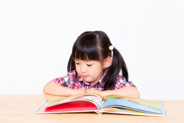 白背景の前で本を読む幼い女の子。幼児、教育、読書、学習、成長、育児イメージ