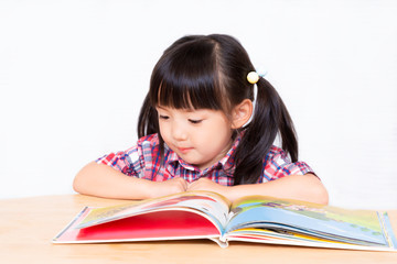 白背景の前で本を読む幼い女の子。幼児、教育、読書、学習、成長、育児イメージ