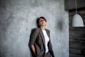  45s years old businesswoman working at office at the background grey wall ,  Entrepreneur wearing a fashion suit and glasses