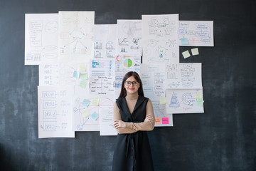 Fototapeta premium Elegant female economist standing by blackboard with flow charts and diagrams
