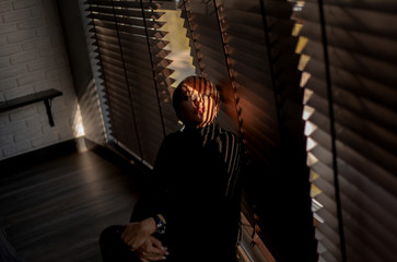 Portrait of beautiful woman in black style clothes posing  on a background of jalousie and brick wall indoors at the house. The sun's beam on eye of a peeking model. The striped shade on the face.