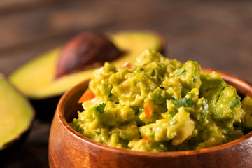 Close-up of guacamole dip bowl and avocados in the background