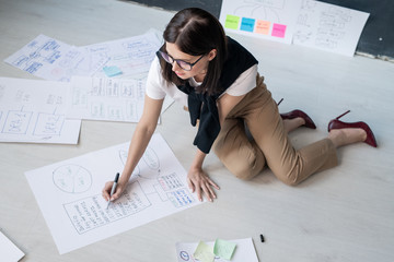 Young female broker in smart casual sitting on the floor and drawing diagrams