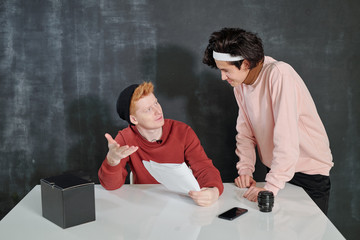 Two young men discussing speech on paper while preparing for video shooting