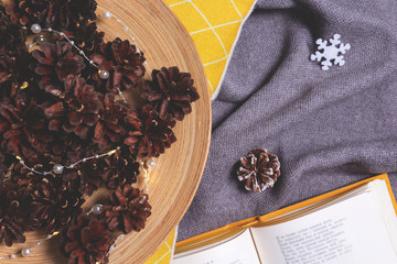 Christmas composition with open book with winter cozy plaid, christmas lights in pine cones. Holiday morning comfort concept. Hygge style. Flat lay, top view.