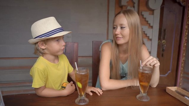 Young woman and her little son eat traditional Balenese food set Nasi Campur in a traditional cafe. Travel to Bali concept. Slowmotion shot
