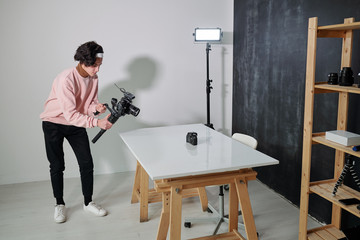Young casual video blogger shooting new photo equipment in studio