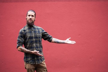 young man with beard and gauged pierced ears pointing in front of a red wall background