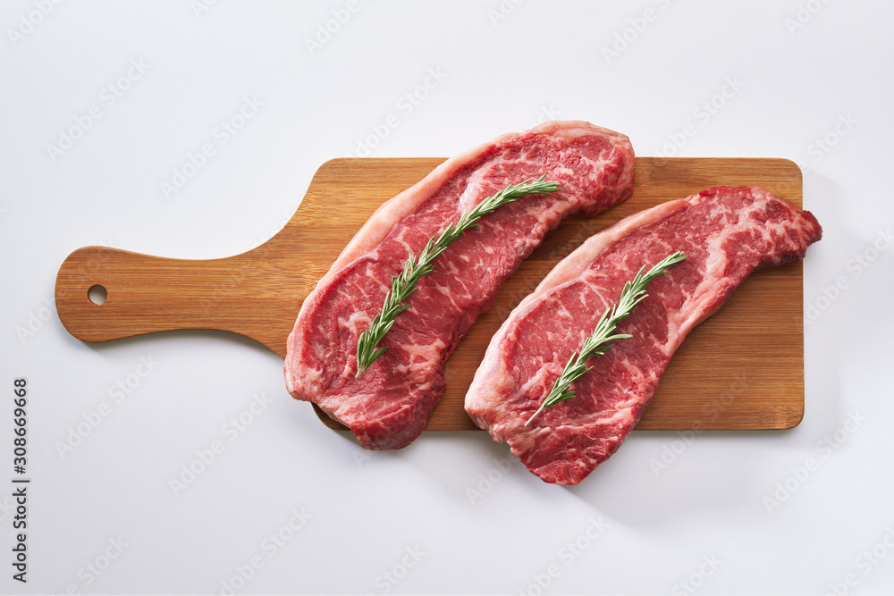 Wall mural raw beef steak ready to be cooked. photo of two fresh raw striploin steak on wooden board on white b