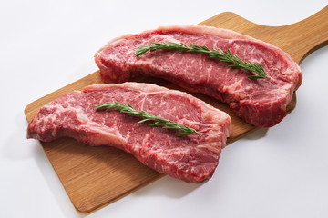 Striploin steaks being prepared for cooking. Two fresh raw beef steak on wooden board on white background with rosmary.