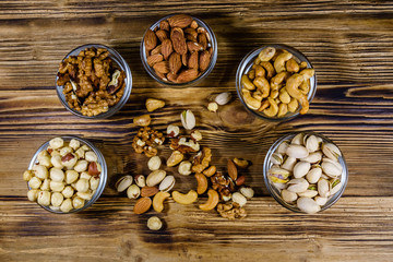 Various nuts (almond, cashew, hazelnut, pistachio, walnut) in glass bowls on a wooden table. Vegetarian meal. Healthy eating concept. Top view