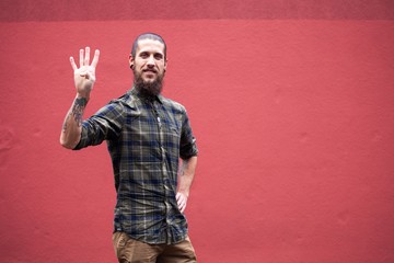 young man with beard and gauged pierced ears counting in front of a red wall background