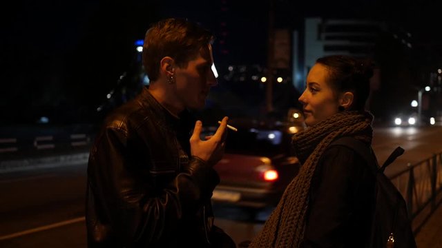 The guy and the girl smoke. Loving couple smokes cigarettes on the street at night.