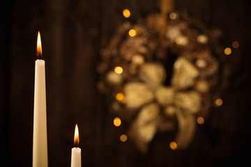 two candles in candlesticks on background Christmas wreath on dark wooden background