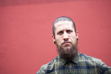 young man with beard and gauged pierced ears on red wall background