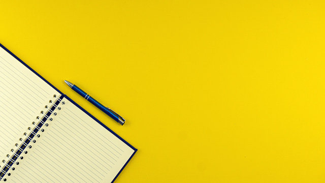 Flat lay top view opened blue notebook agenda with ballpoint pen on yellow background
