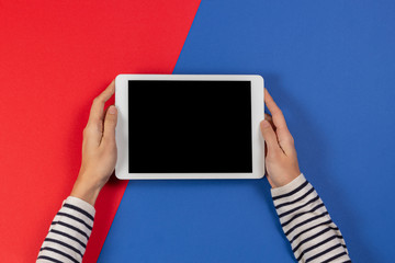 Female hands with tablet computer on blue and red background. Top view