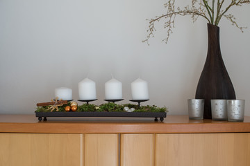 Adventskranz erster Advent mit weihnachtlicher Deko neben Glitzerzweigen in der Vase und Teelichtgläsern