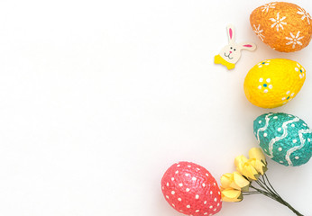 Colorful painted orange, blue, red and yellow Easter eggs with Easter rabbit and yellow spring flowers on white background. Happy Easter holiday. Flat lay style with copy space.