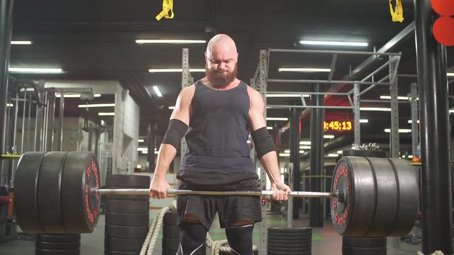 Strong sporty bodybuilder keeping heavy metal barbell in hands doing lifting exercise, energy fitness motivation concept