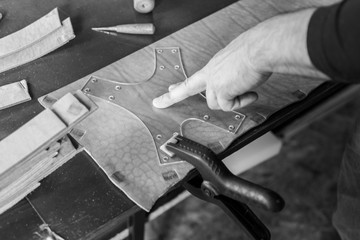 The master working with leather. On brown wooden table scattered with tools and accessories.