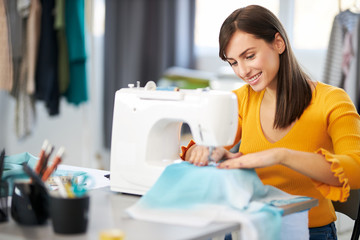 Smiling charming caucasian fashion designer sitting in her studio and sewing beautiful evening...