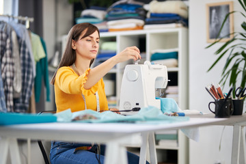 Dedicated seamstress sitting in her studio and insering thread on sewing machine.