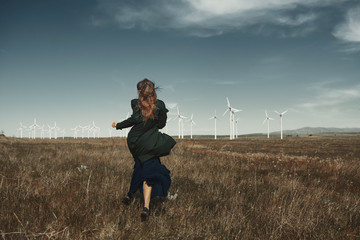 Woman with long tousled hair next to the wind turbine with the wind blowing