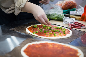 Woman make pizza, sprinkles vegetable toppings on the dough