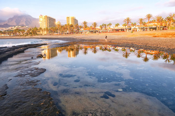 Black volcanic sand on the island of Tenerife, Santa Cruz de Tenerife, Canary Islands, Spain. Beach of Las Americas with views of the sea and the waves on the black sand. The promenade in Playa De Las