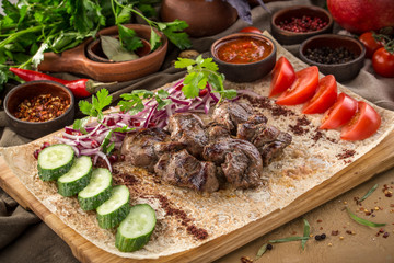 Shish kebab on lavash bread with red onion, tomato, cucumber and tomato sauce on wooden table