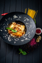 Meat lasagna with beef and tomato sauce on a black plate on a dark wooden background. The concept of Italian cuisine