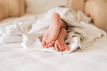 Feet of little sleeping child under white blanket on the bed.