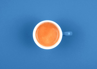 Top view of fresh brewed coffee in ceramic cup on blue background.