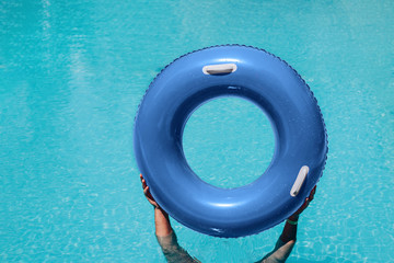Hands holding rubber blue swimming ring above the water in swimming pool.