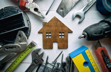 A lot of different rapair equipments on the wooden table and a little wooden house between them