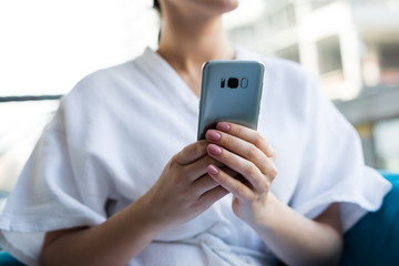 Portrait of beautiful brunette middle age woman using cell phone looking into the window in the clinic after spa procedures