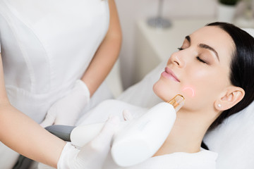 Hardware cosmetology. Face skin care. Skin remodeling. Smiling woman getting facial laser treatment. Dermatologist using laser for skincare treatment of a client removing scars.