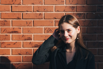 Attractive young girl with red lips and blue eyes touching her brunette hair with her hand, brick wall on the background