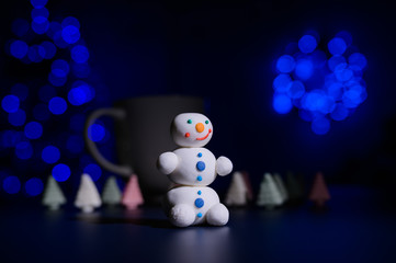 Cute snowman and little Christmas trees made of marshmallows on the background of Christmas lights....