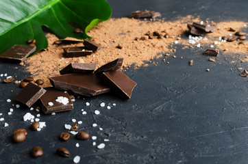 Close up of pieces of dark chocolate, salt, cocoa powder, coffee beans on the dark sufce.Concept of natural salty chocolate.Empty space for design