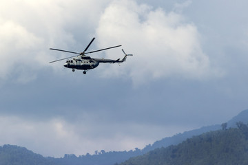 Fototapeta na wymiar Big helicopter flying against the background of mountains, clouds and forest settlement