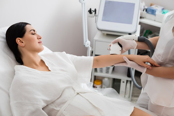 Hardware cosmetology procedure from a therapist. Attractive woman is receiving the laser epilation of her hands in beauty salon.