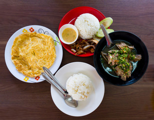 op view composition of various Asian food on wooden table, Hot and Spicy Soup with Pork Ribs, Omelet, Fried pork and Streamed rice.