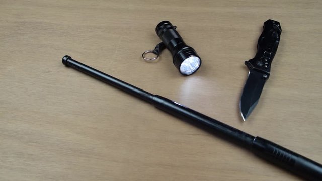 Black knife baton and flashlight on a black surface. Ready for a fight