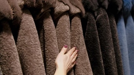 Woman choosing luxury wool warm winter coats for winter sale on a clothes rack in a retail fashion store