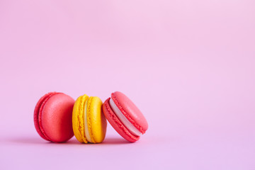 Three tasty french macarons on pink background.  Pink and yellow macarons.